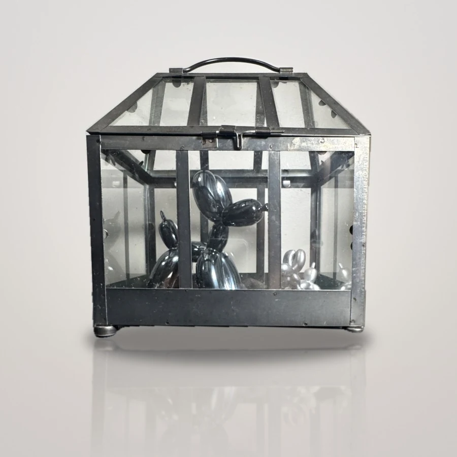 Metal terrarium holding two black balloon-dog sculptures